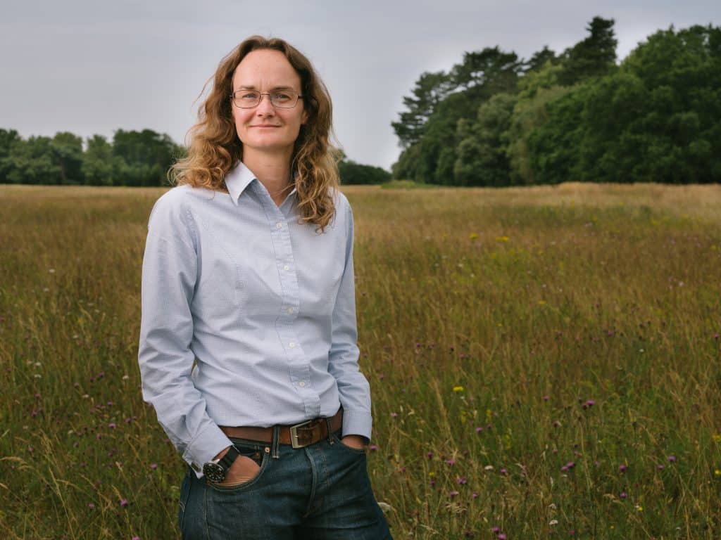 Sue Pendlington Holkham's Sustainability Manager, a white woman with curly brown hair and glasses, wearing a light blue shirt standing in field.